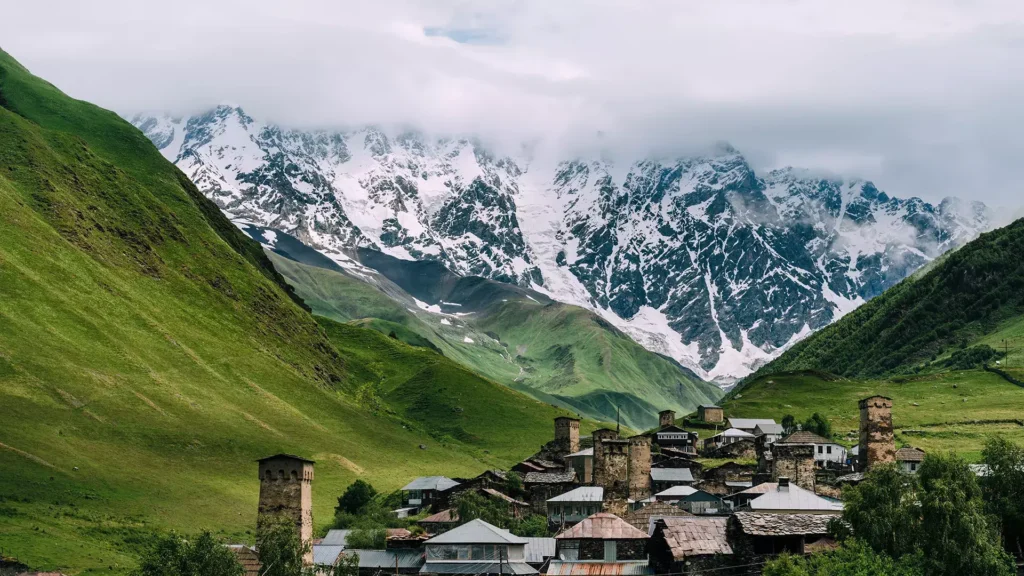 Gergeti Trinity Church on a green hill below snow-capped Caucasus peaks in Georgia